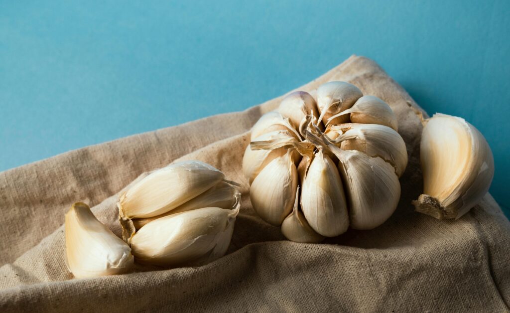Close-up of organic garlic cloves and bulb on rustic burlap with a blue background. Perfect for culinary or organic themes.